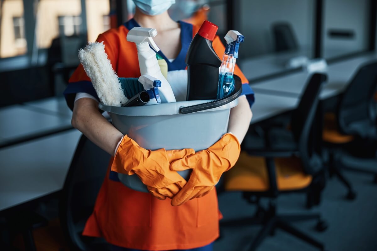 Pracownik trzyma zestaw środków czystości, oferując usługi sprzątające dla firm.