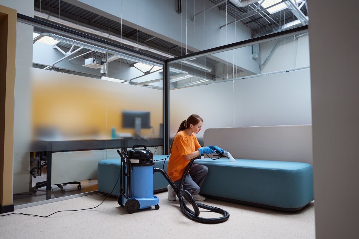 Osoba w pomarańczowej koszulce używa odkurzacza do sprzątania budynków.