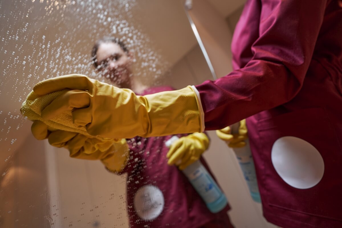 Osoba w żółtych rękawicach myje powierzchnię szkła, wykonując profesjonalne sprzątanie.